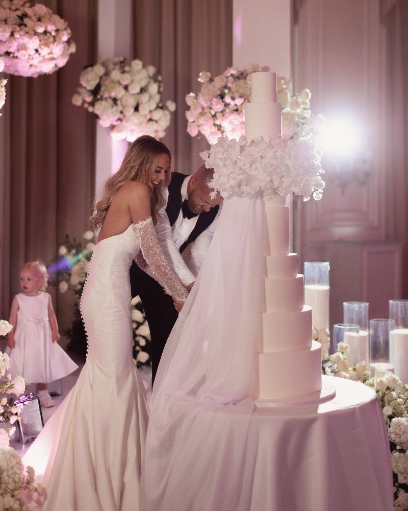 a big white wedding cake getting cut by the bride and groom